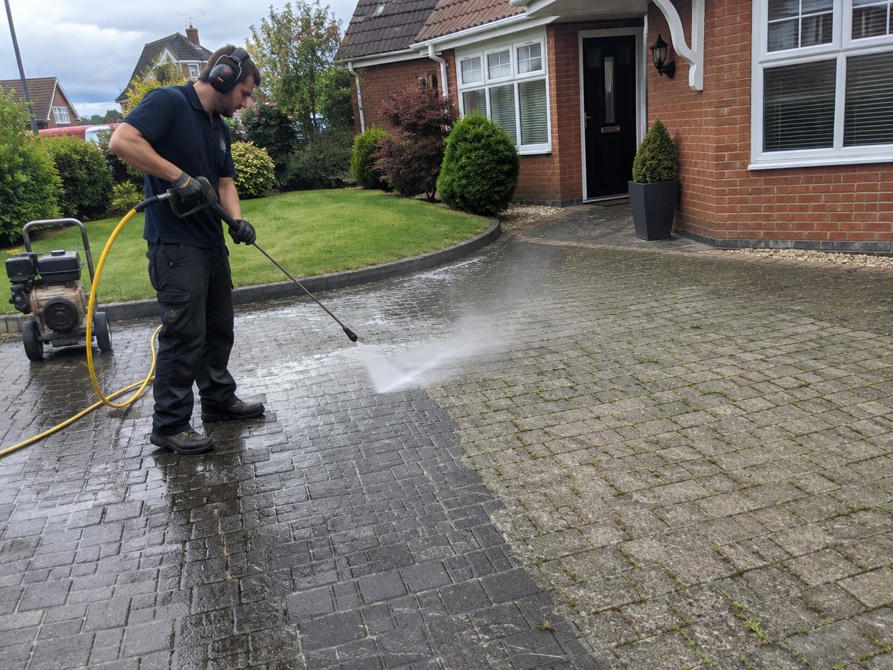 A Gardenscape operative pressure cleaning a block paved Essex driveway, showing the dirty surface next to the clean half
